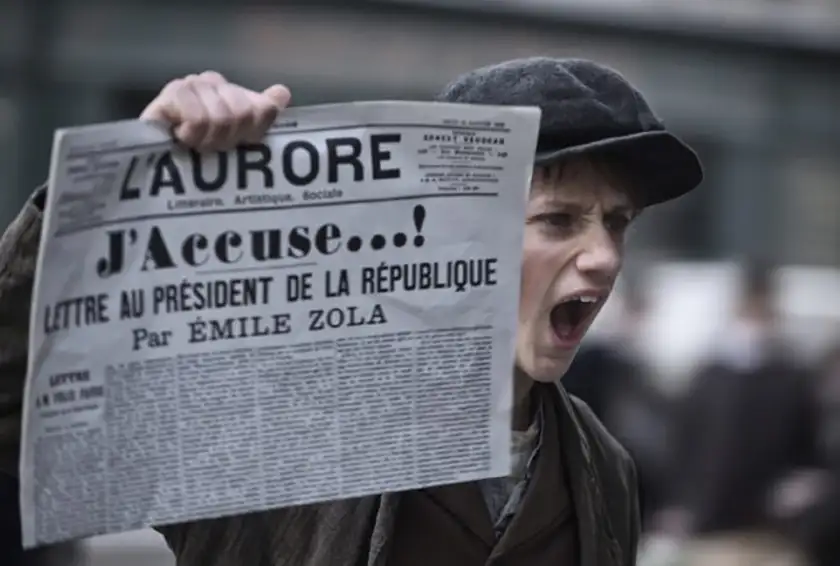 A boy holds a newspaper that reads "J'Accuse" in a still from Roman Polanski's film An Officer and a Spy