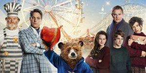 Paddington bear raises his hand holding his hat to say hi in the poster of the film Paddington 2