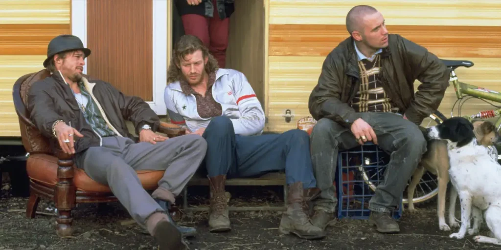 Three men sit outside a trailer in the film Snatch