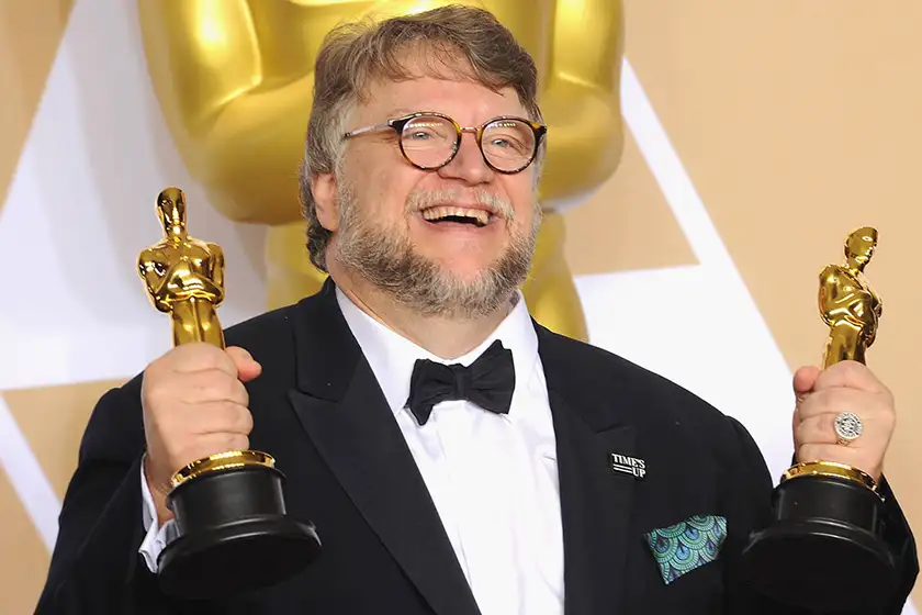 Guillermo del Toro holds two Academy Awards and smiles, in a still featured on a Loud and Clear Reviews article on why the Oscars are taken too seriously