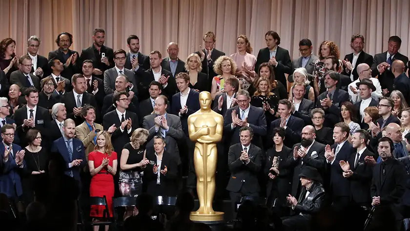 Many creatives pose with a giant Academy Award, in a still featured on a Loud and Clear Reviews article on why the Oscars are taken too seriously