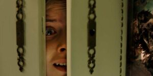 A woman looks terrified from behind a door in a still from Hanna Bergholm’s Hatching