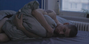 A man hugs a pillow sleeping in his bed in Drifter