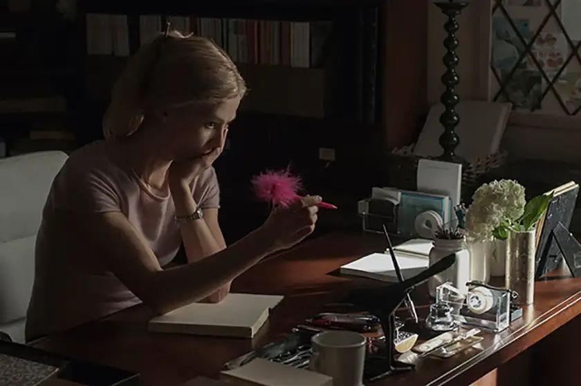 Rosamund Pike sits at a desk in a still from the movie Gone Girl