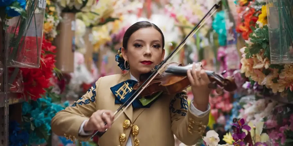 A Mexican woman plays the violin with some beautiful flowers behind her in a still from the film Going Varsity in Mariachi