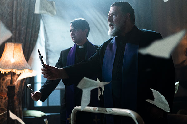 Father Esquibel (Daniel Zovatto) and Father Gabriele Amorth (Russell Crowe) hold crucifixes in THE POPE’S EXORCIST