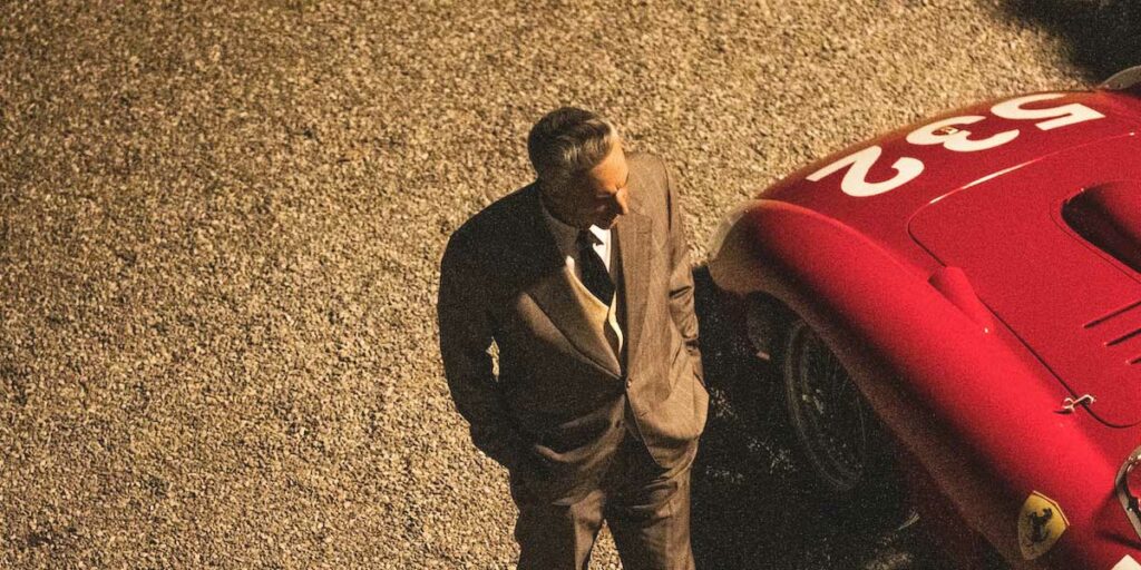 Adam Driver walks next to a Ferrari car, seen from above, in a still from Ferrari