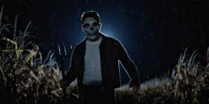 A boy with a painted face stands in a corn field in a still from the film Dark Harvest