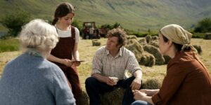 Four people chat outdoors in a field in a still from the film That They May Face The Rising Sun