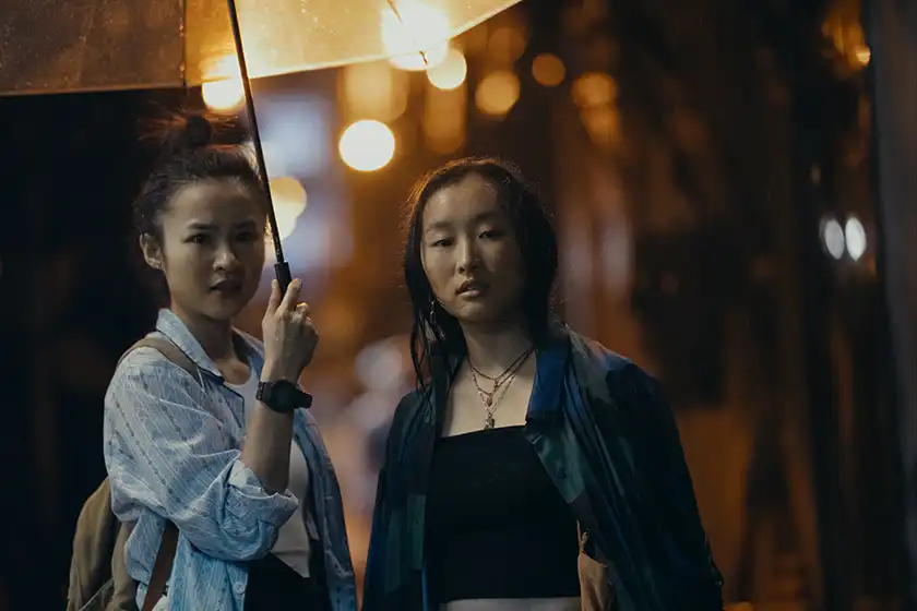 Charly (Bonde Sham) and Mercy (Ji-young Yoo) stand under an umbrella in the series premiere of Expats, reviewed on Loud and Clear Reviews