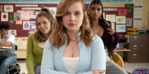 A girl with a blue cardigan looks at the camera with two girls behind her in a still from the 2024 movie remake "Mean Girls"