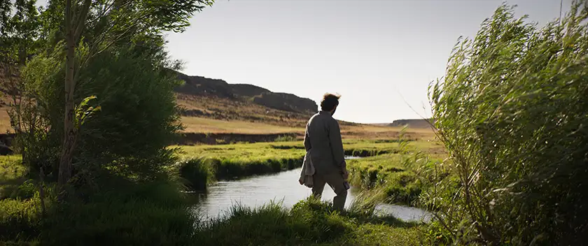 a man looks at a lake surrounded by nature in the film About Dry Grasses