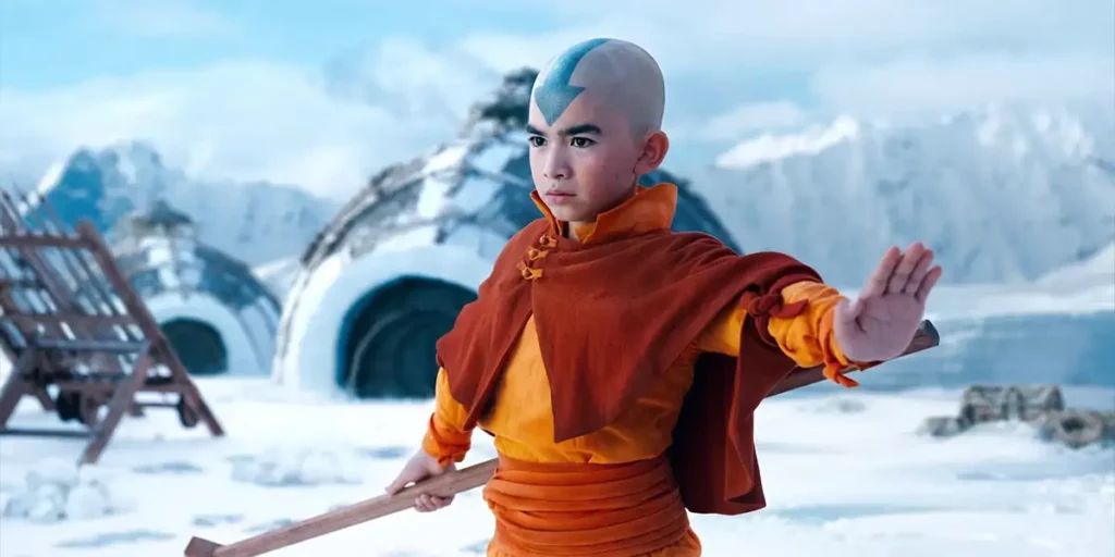 Gordon Cormier as Aang stands in the snow with one hand raised and the other holding a stick in Avatar the Last Airbender (2024)