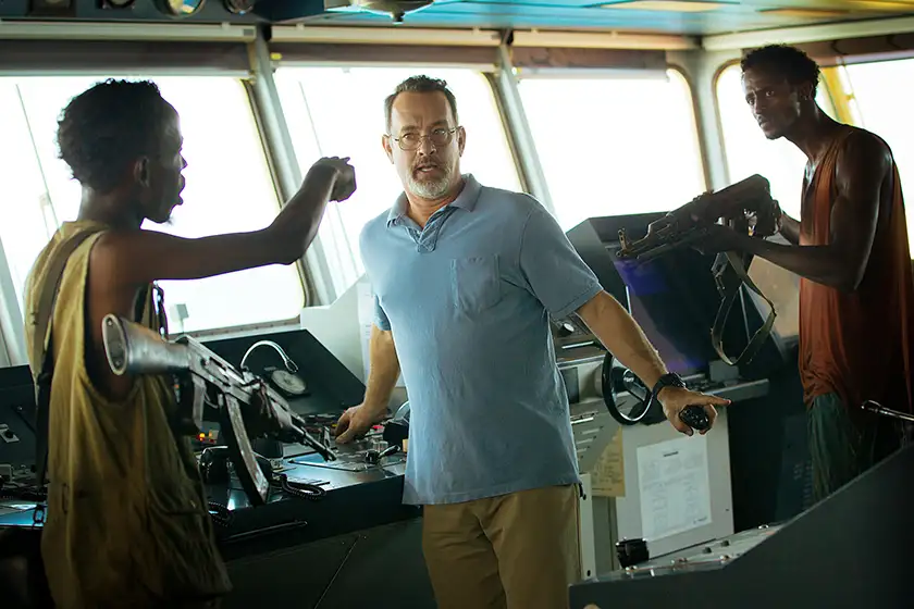 two men point rifles at Tom Hanks inside a boat in the film Captain Phillips
