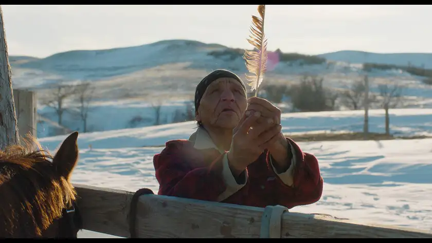 An elderly native lady holds a feather in Pine Ridge under the snow, in the film Eureka from Lisandro Alonso