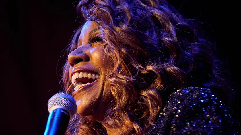 Gloria Gaynor smiles holding a microphone in a still from 2024 film I Will Survive