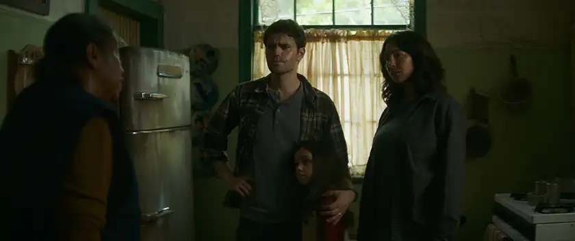 Rhonda Dents as Trudy, Paul Wesley as Ron, Murphy Bloom as Daria, and Jackie Cruz as Alegre stand in a kitchen in Shudder film History of Evi