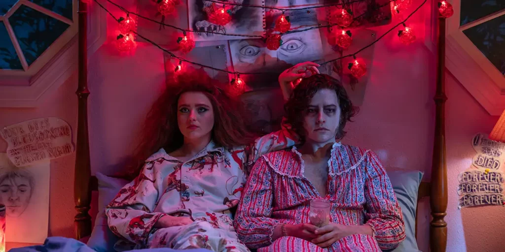 Cole Sprouse (The Creature) and Kathryn Newton sit on the bed looking at the camera in the film Lisa Frankenstein