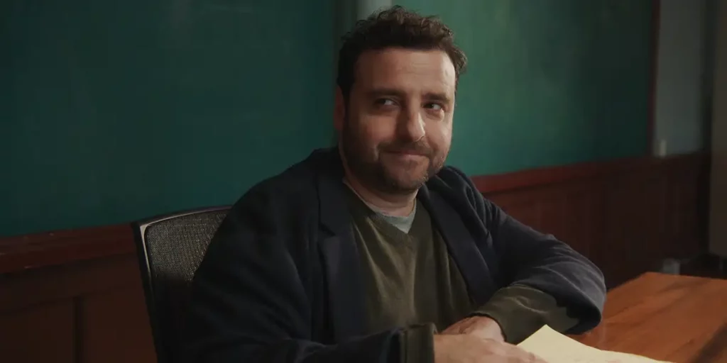 David Krumholtz is at his desk and smiles in the film LOUSY CARTER