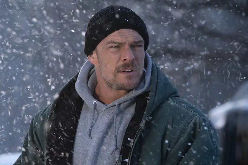 Alan Ritchson stands as “Ed Schmitt” while it's snowing in the film Ordinary Angels