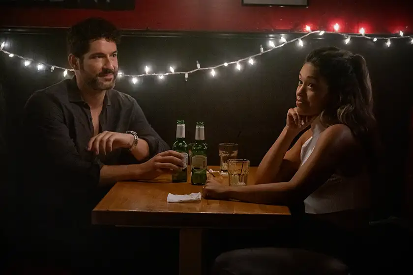 Tom Ellis as Nick and Gina Rodriguez as Mack sit at a table in a romantic mood in the Netflix film Players