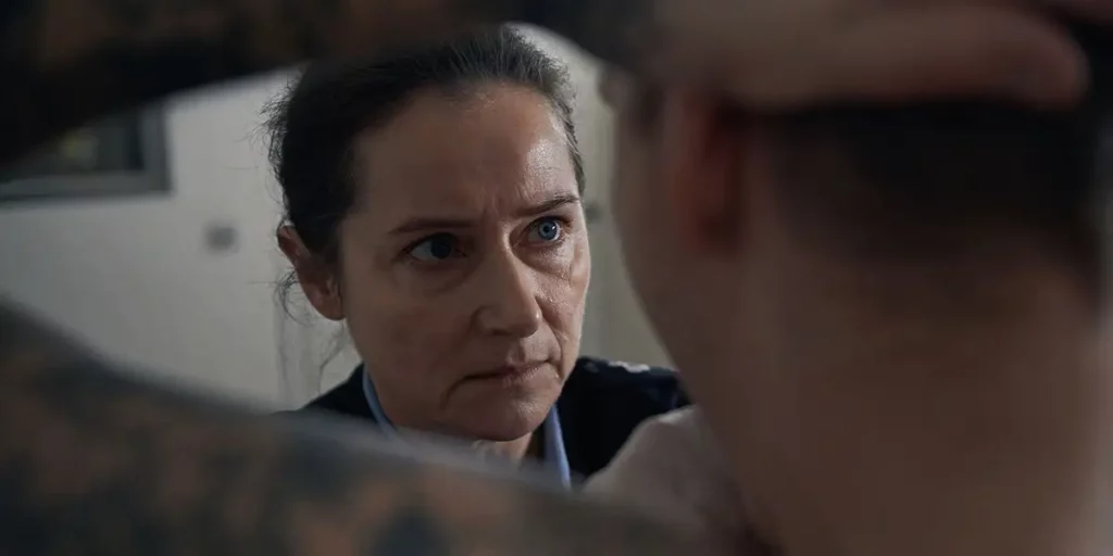 A woman's face is seen in between the raised arms of a naked tattooed man in the film Sons (Vogter) from Gustav Möller