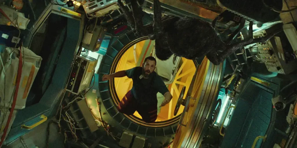 Adam Sandler is in a spaceship, facing a giant spider, in the film Spaceman