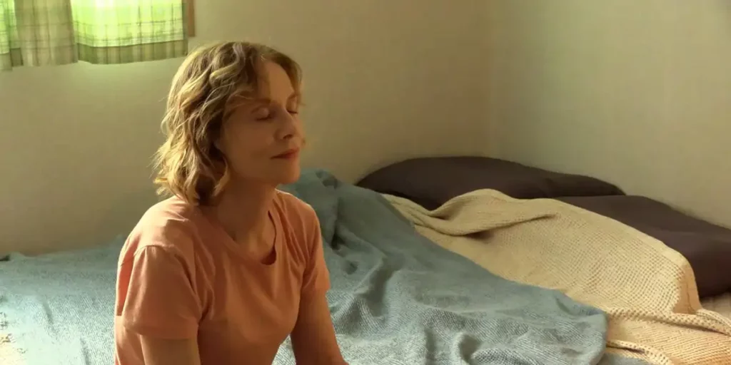 Isabelle Huppert sits on a bed in the film A Traveler's Needs