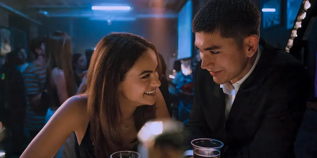 Ana (Camila Mendes) and William (Archie Renaux) flirt while sitting at a table in Prime Video rom-com Upgraded
