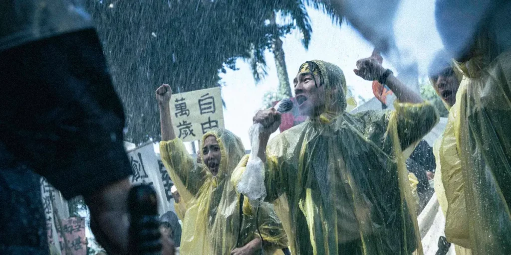 People wear yellow raincoats and shout in the rain during a protest in the film Who'll Stop the Rain