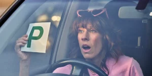 A woman in a car holds up a sign that reads "P" in the film Audrey