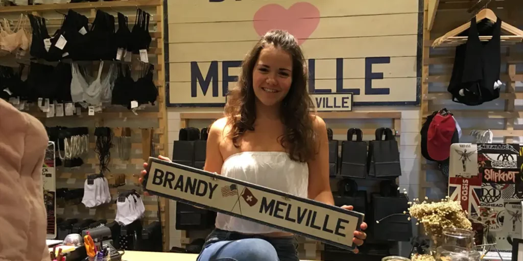 A girl holds a sign with the name Brandy Melville in a store, in the film Brandy Hellville & the Cult of Fast Fashion