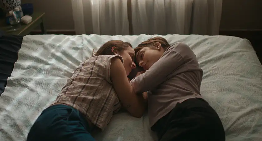 two women hug each other in bed in the film Days of Happiness