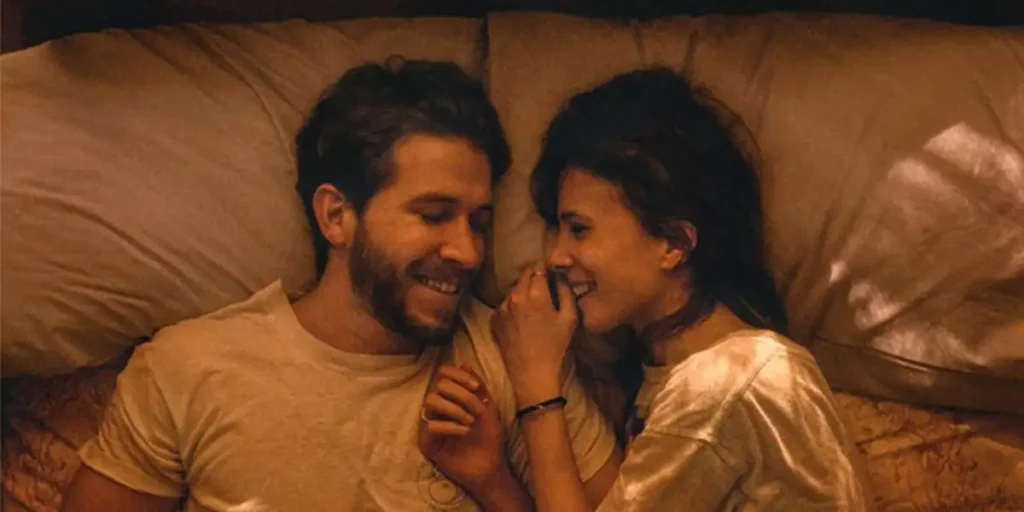 two characters lean close to each other in bed in the film Falling Into Place