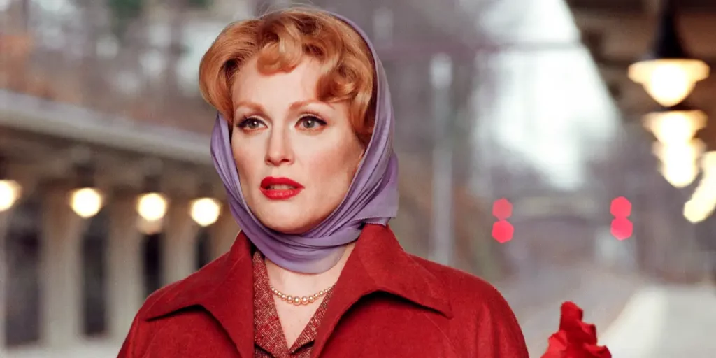 Julianne Moore raises a hand wearing a purple headscarf and a red coat in the film Far From Heaven
