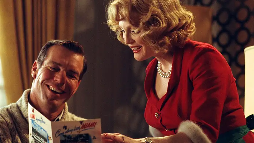Dennis Quaid and Julianne Moore look at a magazine smiling in the film Far From Heaven