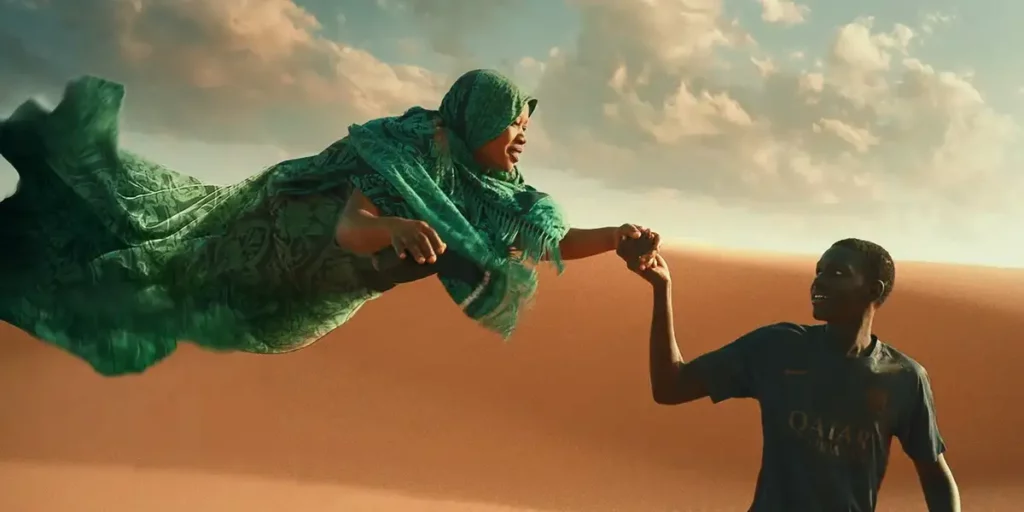 A man holds the hand of a woman in a green dress who's flying in the desert in the 2024 film Io Capitano