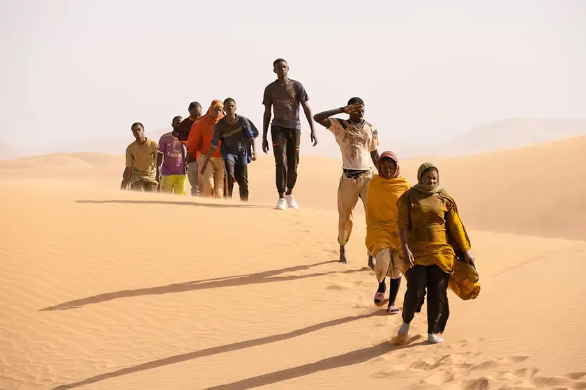 A group of people walk in the desert one in front of the other in the 2024 film Io Capitano