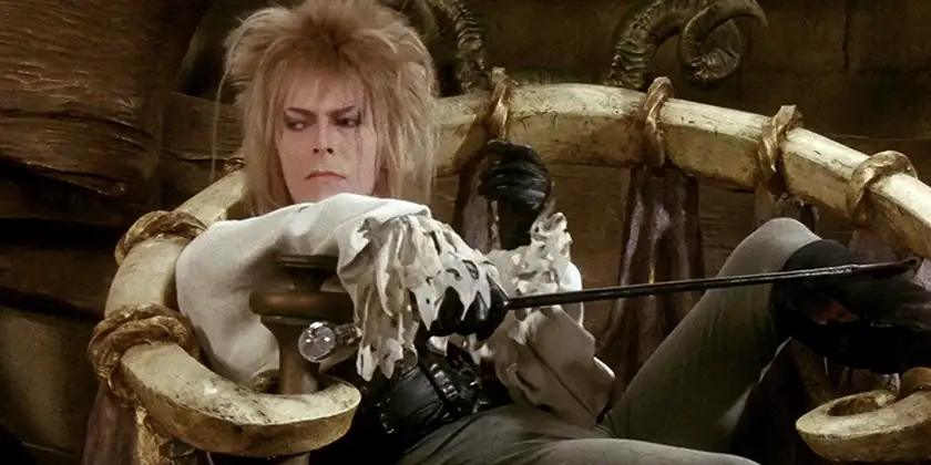 David Bowie - one of 5 Musicians Who Starred in Movies - leans on a chair with a leg raised high in the film Labyrinth