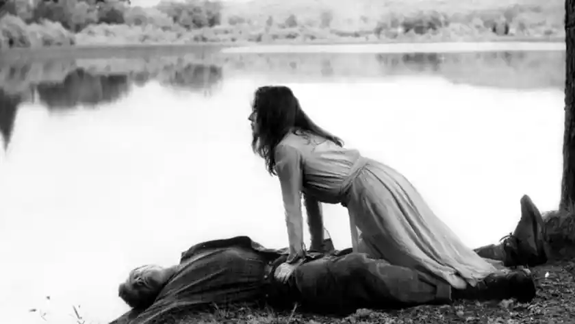 Jeanne Moreau leans on a body by the lake in the movie Mademoiselle (1966)