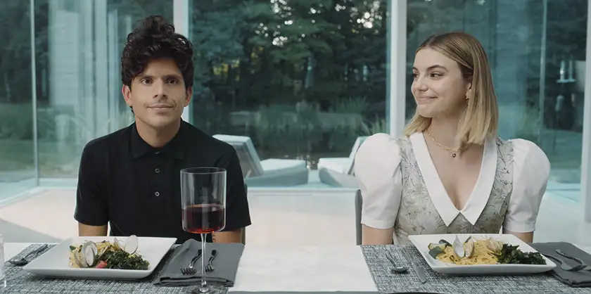 two characters of the Prime Video film Música sit at the dinner table next to each other with seafood pasta in front of them