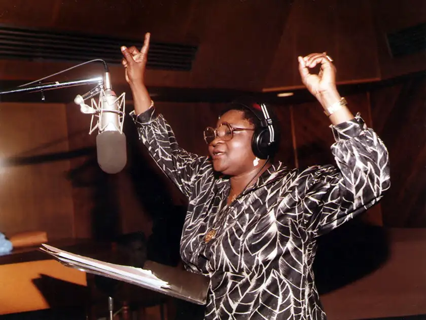Calypso Rose sings with her hands in the air in the new restoration of the film One Hand Don’t Clap