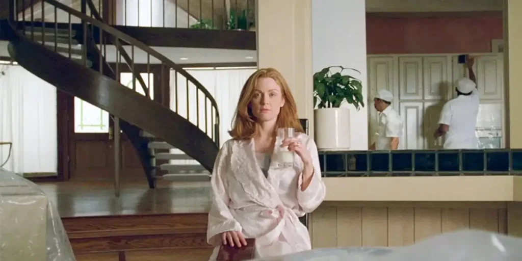 Julianne Moore sits holding a glass, in front of a staircase, in Todd Haynes' 1995 film Safe