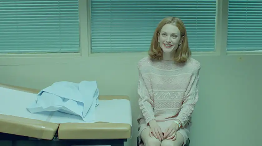 Julianne Moore sits next to a doctor's bed, smiling, in Todd Haynes' 1995 film Safe
