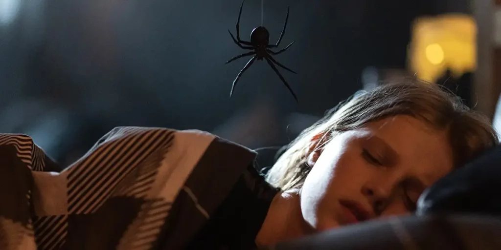A spider looms over a girl's head while she's asleep in bed in the arachnid horror film Sting