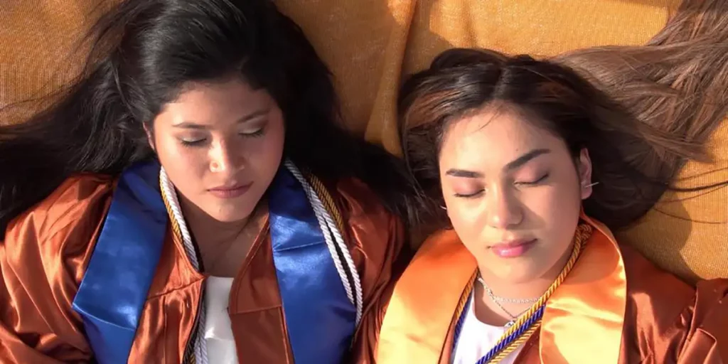 Two girls lie next to each other on an orange blanket with their eyes closed in the documentary film The In Between
