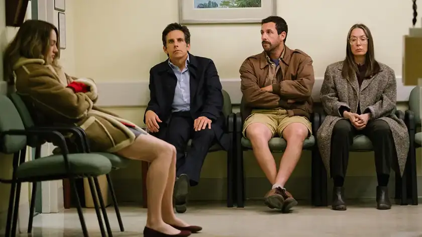 Ben Stiller, Adam Sandler and two women sit on chairs in a waiting room in the film The Meyerowitz Stories