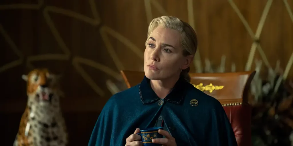 Kate Winslet wears a blue cape and holds a cup of tea with a puzzled expression in season 1 episode 3 of The Regime