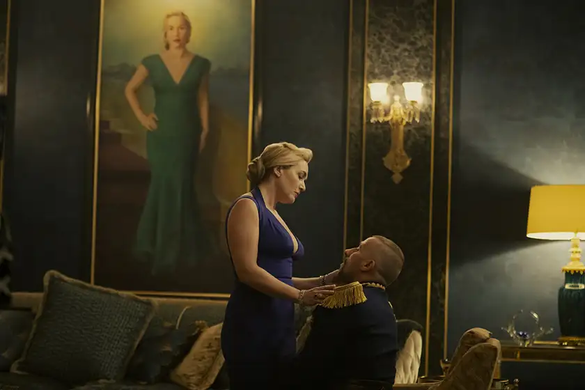 Kate Winslet stands over Matthias Schoenaerts, who sits on the couch, with a painting of herself behind her in season 1 episode 3 of The Regime