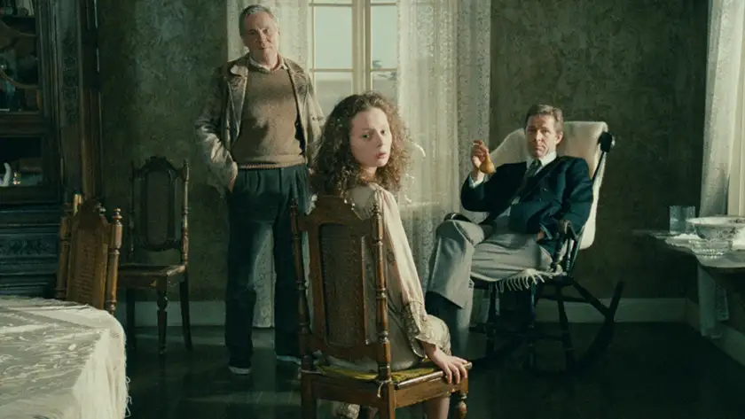 A girl sits on a chair and looks back at the camera, with people behind her, in a still from Andrei Tarkovsky's film The Sacrifice